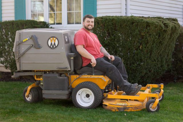 Owner sitting on a ride-on lawn mower used for grass cutting and trimming in Kitchener