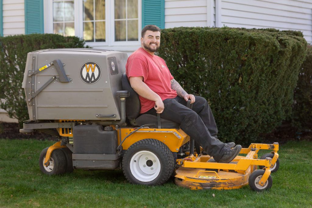 Owner sitting on a ride-on lawn mower used for grass cutting and trimming in Kitchener