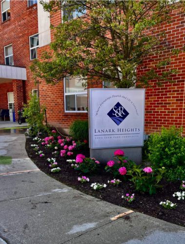 Lanark Heights long-term care community sign surrounded by freshly planted flowers and maintained landscaping.